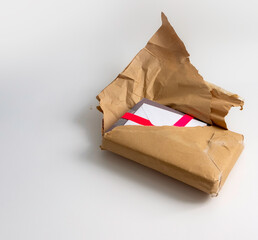 Torn brown postal parcel package revealing wrapped gift or present that is with a pink satin ribbon and a card inside a white envelope. Text space, isolated on white background. Opening gift concept.