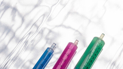 detail of three green, pink and blue syringes, placed at different heights on a silver background