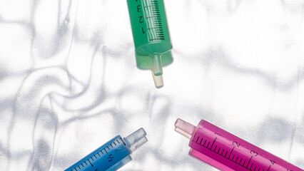 
detail of three green, pink and blue syringes on a silver background