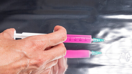 detail of hand with syringe needle with pink injection on mirror background