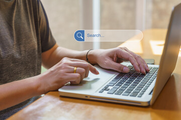 Business and Work From Home and Technology Concept. Asian man using and typing computer laptop with search bar box icon and mobile smartphone on wooden table..