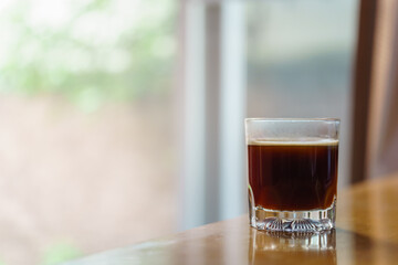 Closeup of glass of hot black coffee Americano with sunlingt and shadow on wooden table with copy space.