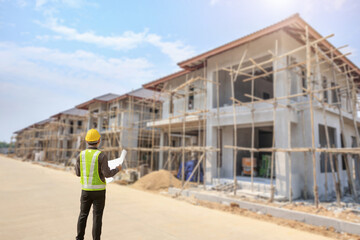 young professional engineer in protective helmet and blueprints paper at the house building construction site