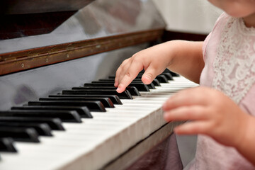 Fototapeta premium A little girl presses her fingers on the white keys of the piano. Teaching children at a music school.