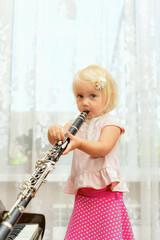 A little girl blows the clarinet and closes the chord switching holes with her fingers.