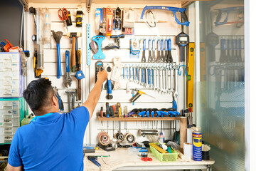 Mechanic taking tool from wall behind his workbench, view from te back