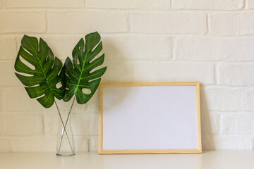 A home workplace.An empty picture frame or photo and monstera leaves in a vase are on the table. Scandinavian style.