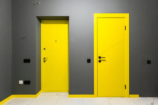 two yellow doors with black handles, on a gray wall