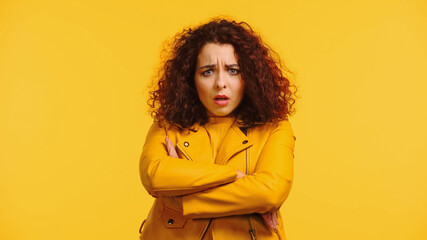 displeased young woman in leather jacket standing with crossed arms isolated on yellow