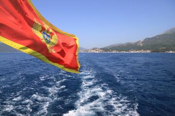 Flag with coat of arms of Montenegro flies over Kotor Bay, beautiful landscape. Summer vacation, tourism in Montenegro, Adriatic Sea