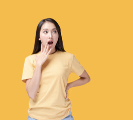 Happy Asian woman wearing yellow t-shirt standing over yellow background. Young Asian woman putting hand over her mouth with surprise face. Portrait of happy Asian female .
