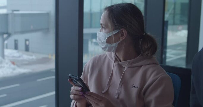 Woman in protective mask uses phone waiting for flight