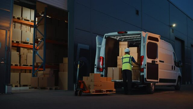 Outside of Logistics Distributions Warehouse Delivery Van: Worker Unloading Cardboard Boxes on Hand Truck, Online Orders, Purchases, E-Commerce Goods, Food, Medical Supply. Evening Wide Static Shot