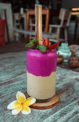 Smoothie in the glass with straw, frangipani flower and sliced strawberry on the wood table background. Healthy dessert.