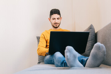 Mid adult man working remotely from the sofa at home. Concept of future, family balance and home workspace.