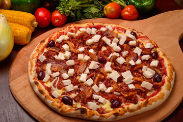 Heart of palm pizza with bacon on a wooden board and vegetables in the background.