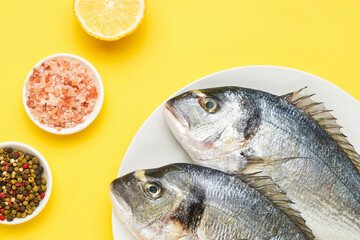 Raw dorado fish with spices on a white plate on a yellow background. Mediterranean seafood concept