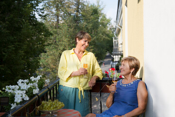 Obraz premium Portrait of happy senior woman friends standing on the balcony of the apartment with wine glasses 