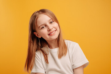 Beautiful little girl looking at the camera and smiling isolated on yellow background with copyspace. Cute teen kid portrait