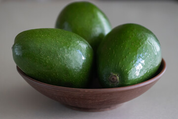 Green avocado in a brown plate on a light background.