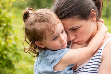 Little girl in denim dress in the arms of her sad mom