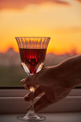 A man's hand with a glass of red wine on the background of a bright sunset.