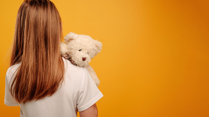 Little girl child with teddy bear isolated on yellow background with copyspace. Horizontal portrait...