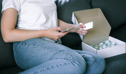Online shopping using the application on the phone. A faceless woman sits in bed unpacks an order and holds a smartphone and a credit card.