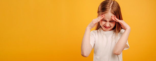 Beautiful little girl thinking and holding her hands on her head isolated on yellow background with copyspace. Kid with funny face expression during professional photoshoot