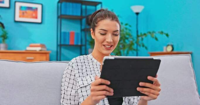 Student studying in a foreign city, sitting on the couch in the dormitory, relaxing after classes, holding a tablet in hand, talking via video camera, the Internet with parents, telling stories