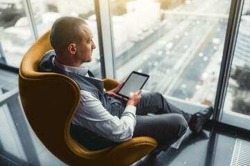 A side view of a man entrepreneur with a digital tablet pc in his hands is sitting on an orange...
