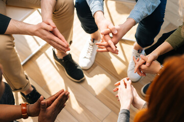 Close-up top view of group diverse multiethnic people sitting in circle with hands crossed hands together during business meeting. Closeup top view multiracial people analysing share mental problems.