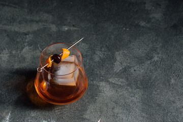 bourbon whiskey old fashioned cocktail with large ice cube and cherry orange on gold cocktail pick 