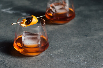bourbon whiskey old fashioned cocktail with large ice cube and cherry orange on gold cocktail pick...