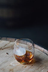 dram of whiskey in a glass with sphere spherical ice on wood barrel 
