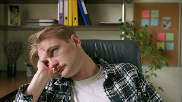 Young guy has woken up after sleeping, sitting in chair. Close up portrait