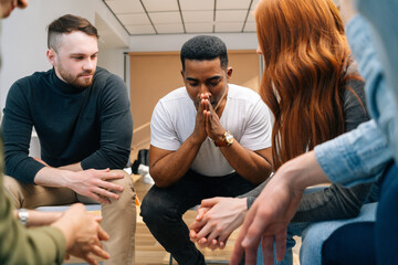 Front view of depressed African American young man sharing problem sitting in circle on group...