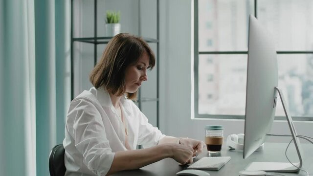 Lady in blouse takes off glasses at computer in office