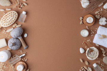 Spa treatment with cosmetic bottle, candles and herbal bag, towel on brown background. Flat lay, copy space.