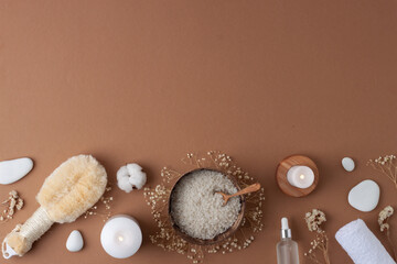 Spa treatment with cosmetic bottle, candles and towel on brown background. Flat lay, copy space.
