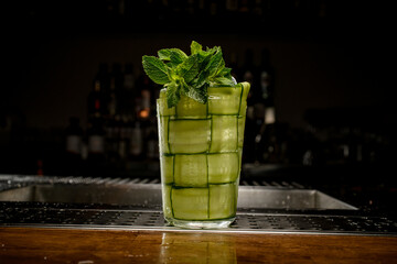front view of glass with cocktail garnished with mint and slices of fresh cucumber