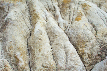 Close-up of a hillside made of gray-yellow clay. Vertical folds of the surface, erosion results and cracks. Lifeless and desolate landscape. The image can serve as a texture or background.
