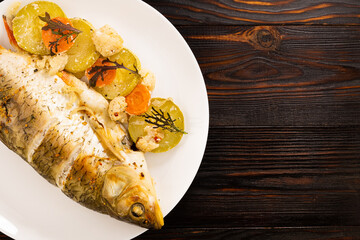 baked fish with vegetables on a wooden background. Top view with copy space