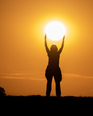 Silhouette of a woman in a field trying to catch the sun at sunset.