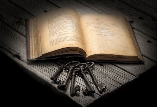 Libro antiguo abierto y con un juego de llaves en primer plano sobre la mesa de madera an tigua.