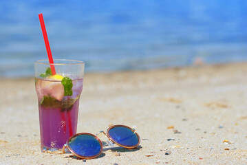 A glass with pink lemonade on the sand and sunglasses. Summer landscape on vacation. Beach vacation.
