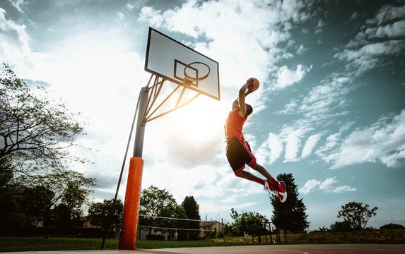 Street basketball player making a powerful slam dunk on the court - Athletic male training outdoor at sunset - Sport and competition concept	
