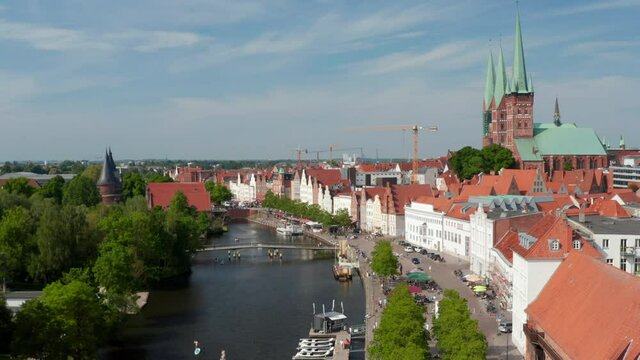 Forwards descending footage of Trave waterfront with moored boats, restaurant terraces and people walking along river. Historic city centre. Luebeck, Schleswig-Holstein, Germany