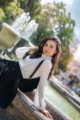Fototapeta premium Portrait woman wear white blouse and black skirt near the public fountain