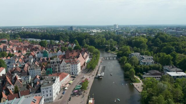Aerial view sunshades on terraces of waterfront restaurants. Wide street along Trave river and historic old town. Luebeck, Schleswig-Holstein, Germany